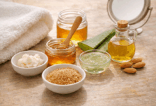 Ingredienti naturali per la cura delle labbra su tavolo in legno chiaro: miele, burro di karité, aloe vera, zucchero di canna e olio di mandorle con asciugamano bianco in luce naturale