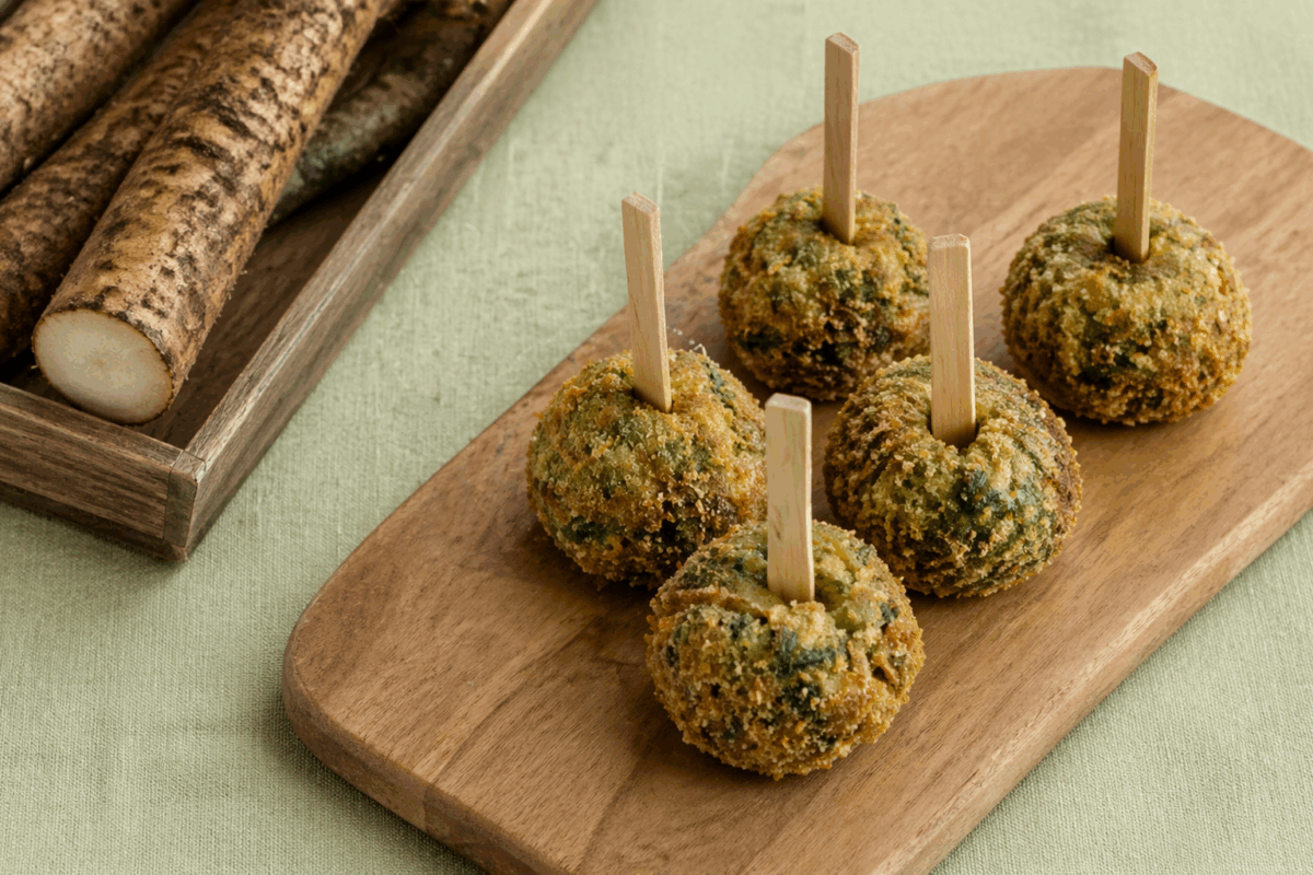 Crocchette di bardana croccanti su tagliere di legno con stecchini di bambù, tovaglia in lino verde e radici fresche a lato
