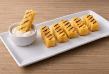 Bastoncini di polenta grigliata con righe dorate serviti su piatto bianco con salsa allo yogurt, ricetta antispreco con avanzi di polenta.