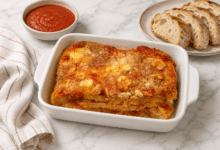 Lasagna rustica di pane raffermo con mozzarella e pomodoro servita in pirofila da forno su piano in marmo con pane casereccio e passata di pomodoro
