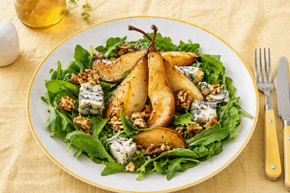Insalata con pere caramellate, gorgonzola e noci servita in piatto bianco con bordo giallo su tovaglia di lino giallo con posate abbinate