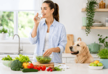 Donna che beve acqua in una cucina luminosa mentre prepara verdure fresche accanto a un cane domestico, simbolo di prevenzione della Giardia e igiene alimentare