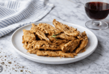 Petto di pollo grigliato servito su piatto di porcellana bianca su piano in marmo con bicchiere di vino rosso e canovaccio a righe azzurre