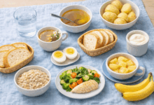 Tavola con alimenti consigliati per la diverticolite: acqua, tisana, brodo, patate lesse, pane bianco, yogurt, uova, verdure cotte, avena, mele cotte, banane e pesce magr