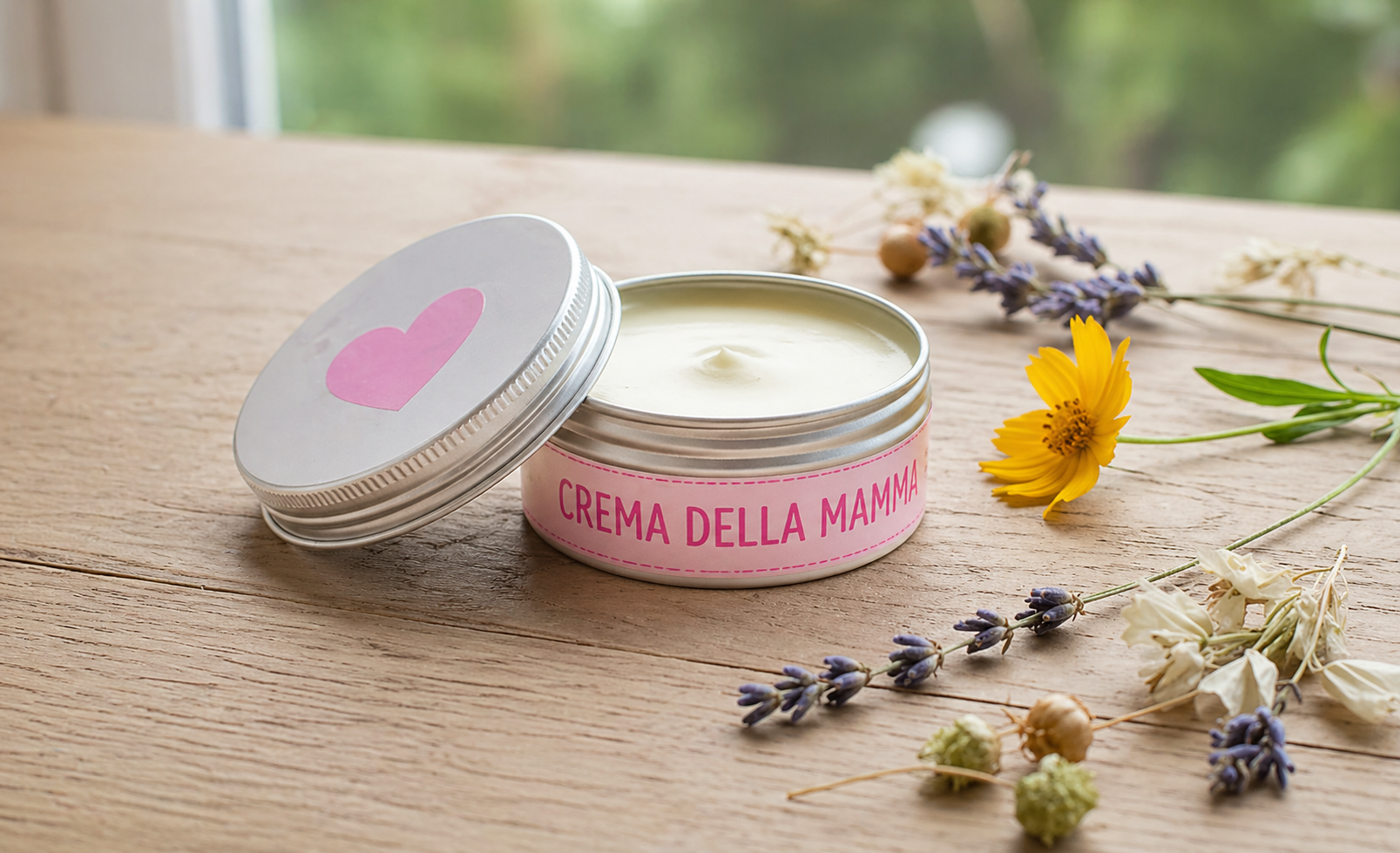 Crema al burro di karité fai da te per la Festa della Mamma in barattolo con etichetta rosa “Crema della mamma” su tavolo in legno con fiori naturali