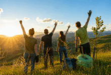 Persone nella natura al tramonto con le braccia alzate durante un’attività di tutela ambientale per la Giornata della Terra