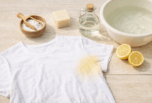 Maglietta bianca con alone giallo di sudore e rimedi naturali come bicarbonato, limone, sapone di Marsiglia e aceto su tavolo in legno chiaro