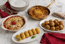 Piatti con ricette anti spreco di Pasqua su tavolo in marmo con frittata, crocchette, polpette e crumble alle fragole con tovaglioli rossi e stoviglie