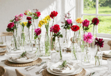 Tavola apparecchiata con bottiglie di vetro e fiori colorati come centrotavola davanti a parete bianca con finestra