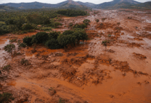 Vista aerea del disastro della diga di Mariana in Brasile con case sommerse dal fango tossico, vegetazione devastata e paesaggio contaminato dai residui minerari.
