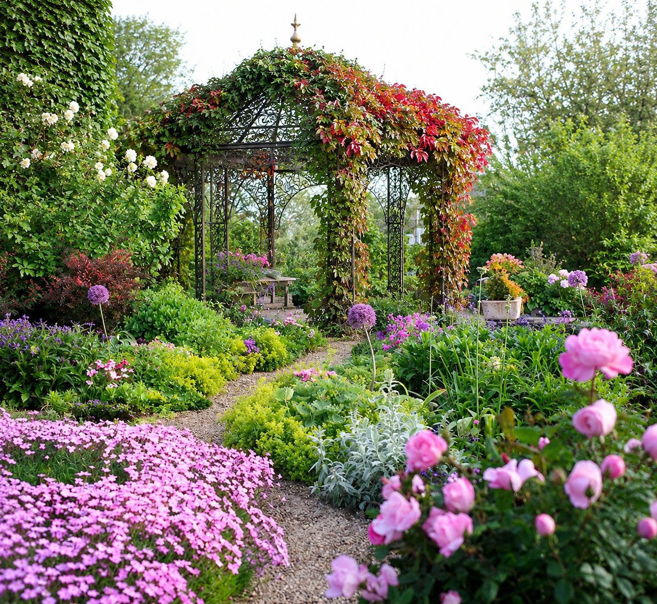 Giardino in stile cottage garden con gazebo in ferro battuto coperto da vite americana, aiuole fiorite e sentiero curvo in ghiaia