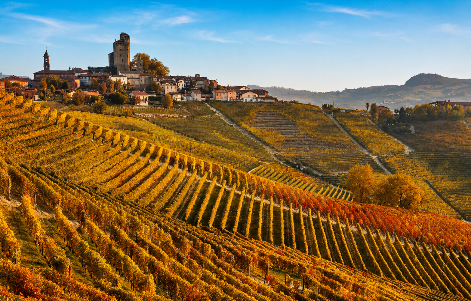 Panorama autunnale delle Langhe con vigneti dorati, borgo collinare e cielo azzurro limpido, ideale per il turismo slow e l’enoturismo in Italia