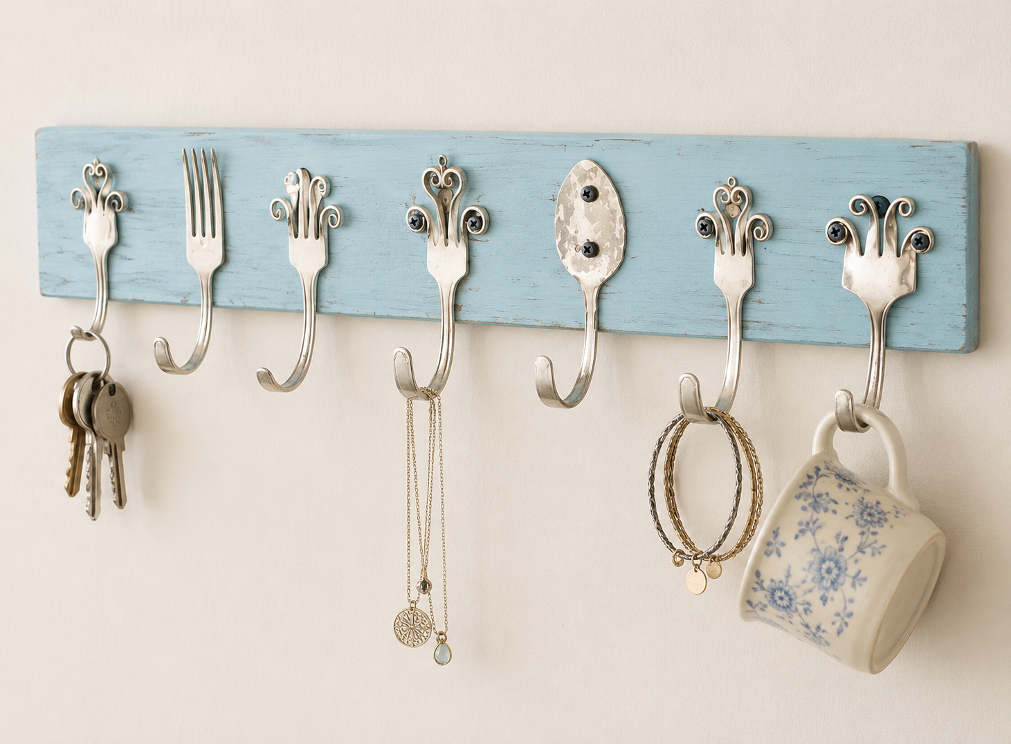Doga azzurro chiaro con posate riciclate trasformate in appendi-tutto decorativi, usate per appendere chiavi, collane, braccialetti e una tazza su parete bianco-beige