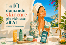 Donna che applica una crema viso in un bagno luminoso affacciato sul mare, con prodotti skincare e smartphone con assistente AI, per illustrare le 10 domande più richieste sull skincare all’intelligenza artificiale.