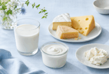Bicchiere di latte, yogurt e formaggi su tovaglia di lino azzurro chiaro, immagine di copertina per un articolo sulla differenza tra allergia alle proteine del latte e intolleranza o malassorbimento del lattosio