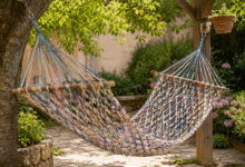 Amaca fai-da-te realizzata con vecchie T-shirt intrecciate, sospesa in giardino tra un albero e un supporto in legno, con rete colorata a nodi e bastoni di sostegno