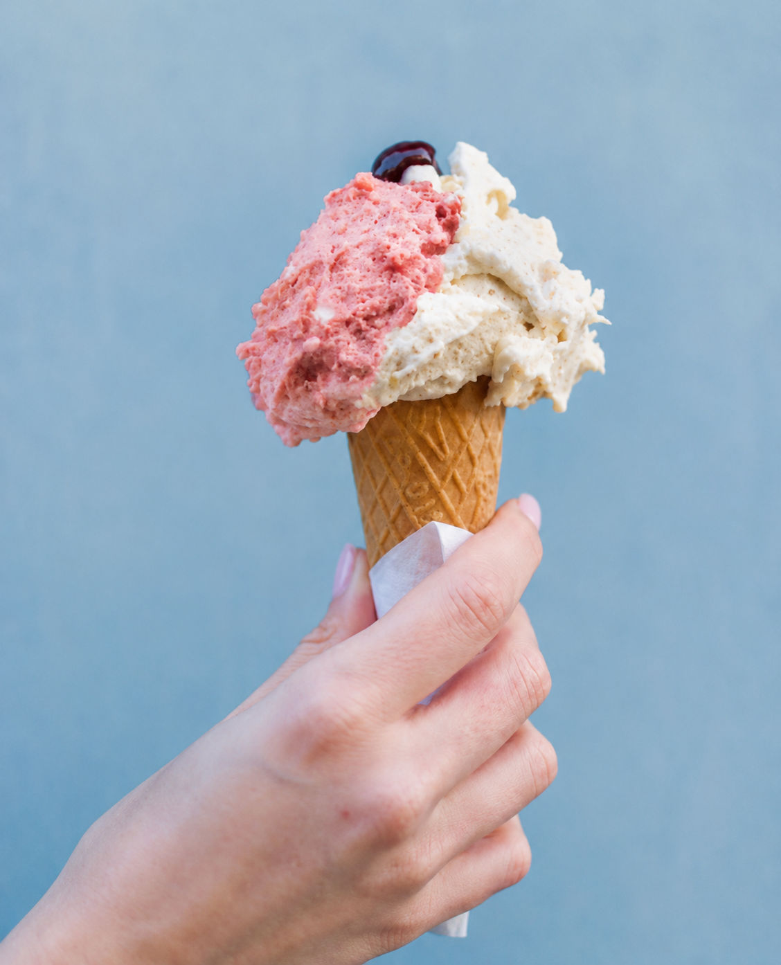 Mano che tiene un cono gelato con una pallina alla fragola e una alla crema poco calorico