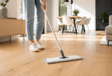 Persona in piedi che pulisce un pavimento in parquet chiaro con un mop e panno in microfibra, in una casa moderna luminosa ed elegante con arredi minimal e luce naturale.