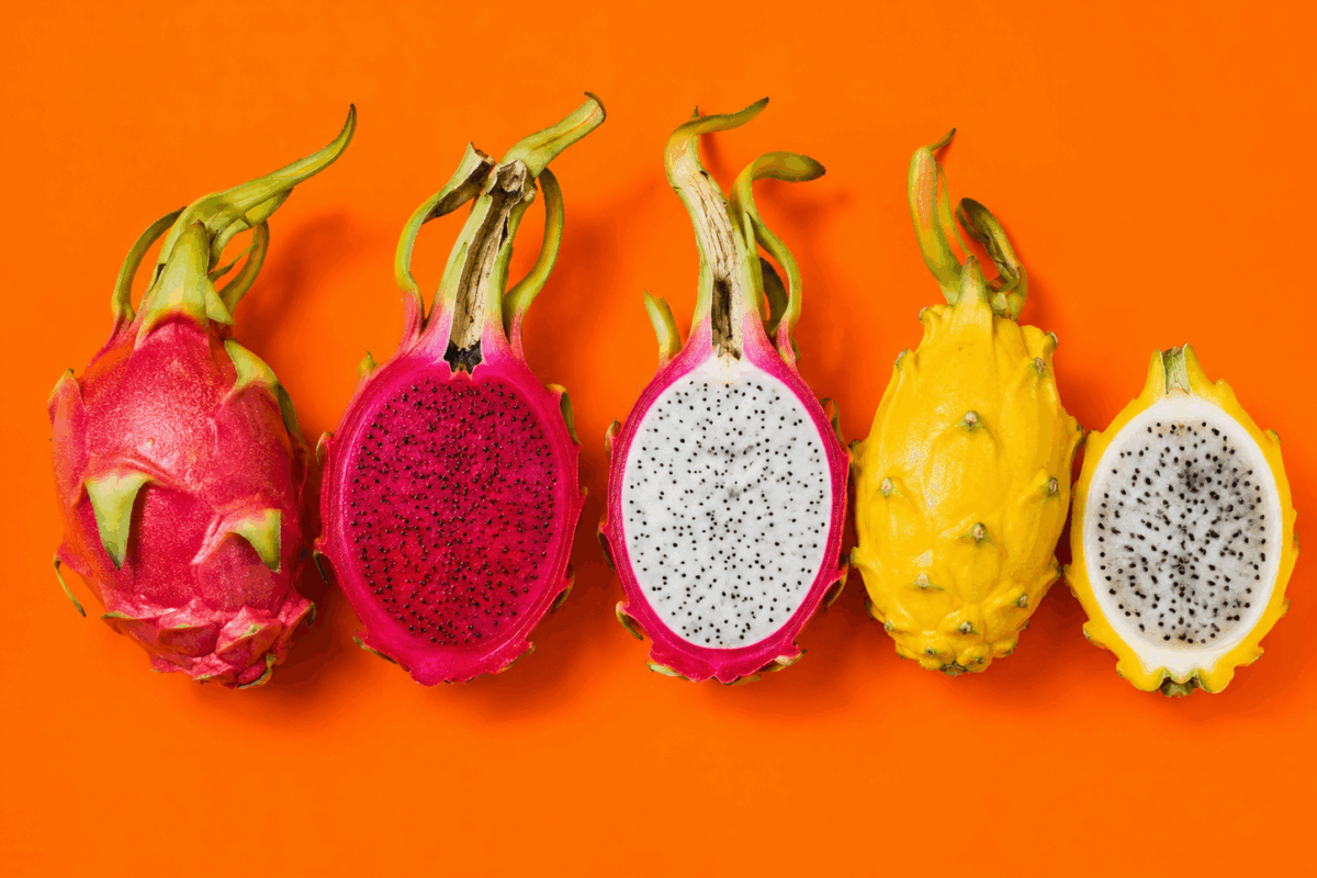 Alcuni frutti del drago su sfondo arancione fluo con una pitaya rossa intera, una a polpa rossa tagliata a metà, una a polpa bianca tagliata a metà, una pitaya gialla intera e una gialla a metà con polpa bianca