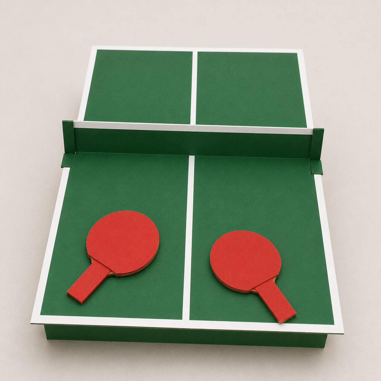 Set da ping pong fai da te realizzato con cartone riciclato, con campo verde e linee bianche, rete in cartone piegato e due racchette rosse appoggiate sul tavolo